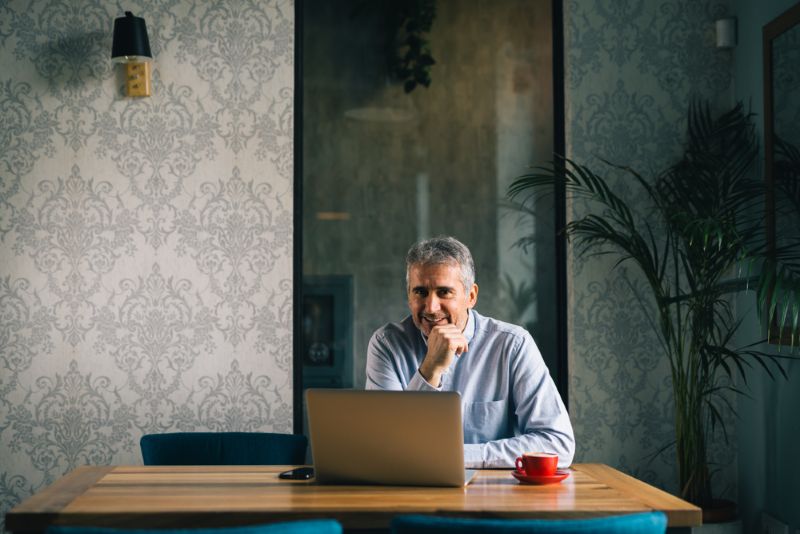 Older man sitting and smiling at his laptop at home